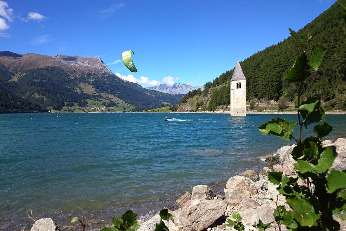 Kitesurfen auf dem Reschensee: Der Stausee bietet von Mai bis Oktober optimale Verhältnisse – auch für Anfänger. Auf den umliegenden Wiesen wird mit dem Kite geübt, bevor es ins Wasser geht. Hingucker ist der aus dem Wasser ragende Kirchturm des ehemaligen Dorfes.