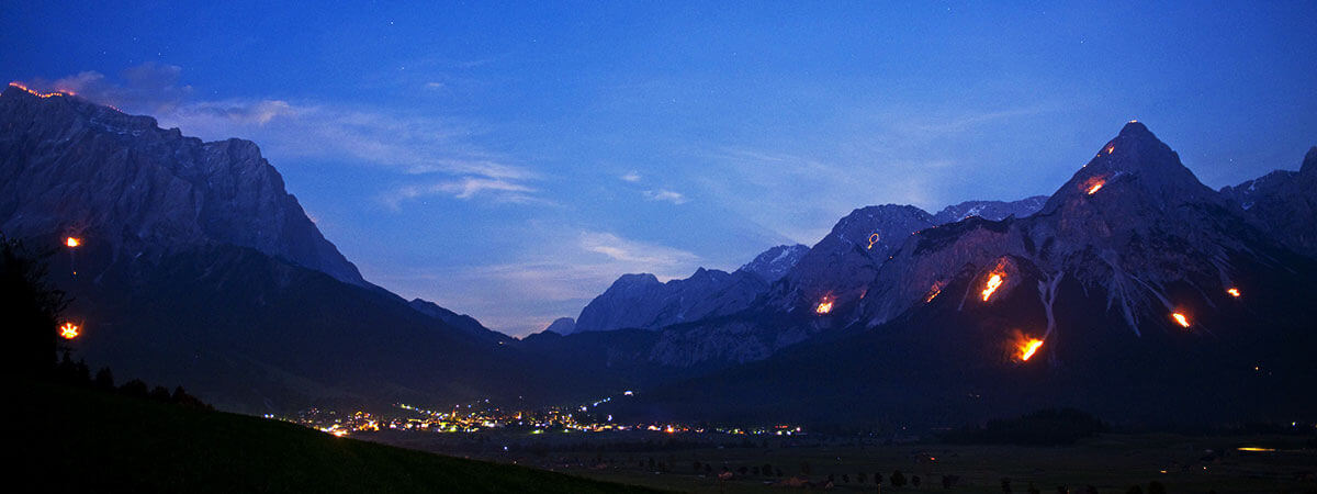 Berge in Flammen – Herz-Jesu-Feuer. Am 24. Juni 2017 verzaubern Feuermotive die Berge der Tiroler Zugspitz Arena bei den traditionellen Sonnwendfeuern