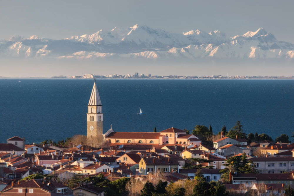 Die Kirche St. Georg über den Dächern von Piran, mit Blick auf die Adria und das winterliche Alpenpanorama. Copyright: Jaka Ivančič