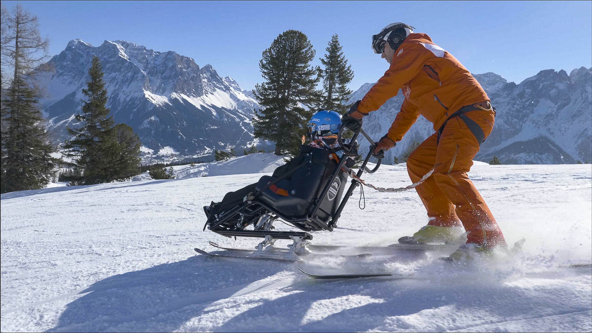 Skilehrer steuert einen Bi-Ski mit einem Gast mit Behinderung über eine präparierte Skipiste in Tirol.