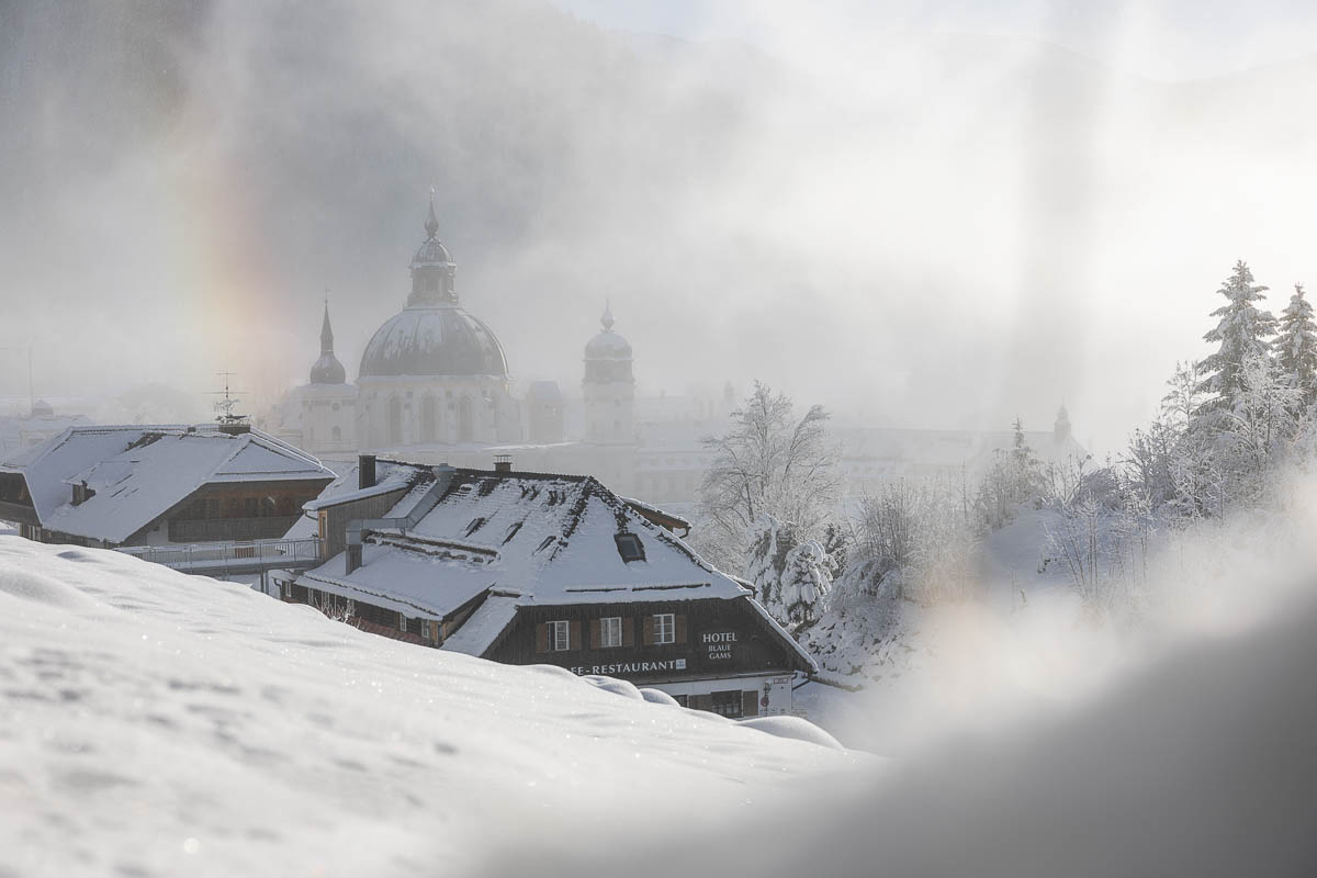 Kloster Ettal im Winternebel mit schneebedeckten Dächern in den Ammergauer Alpen.