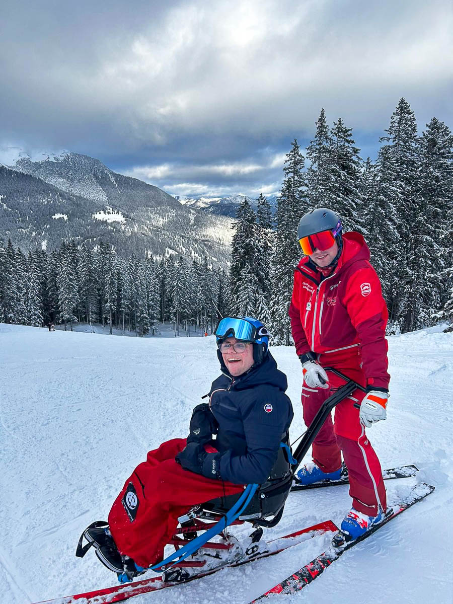 Skilehrer der Skischule Snowpower steuert einen Bi-Ski mit einem Gast mit Behinderung auf einer Piste in Lermoos in der Tiroler Zugspitz Arena.