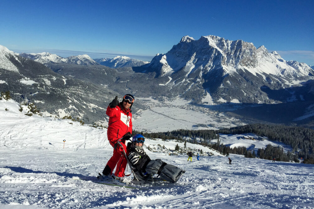 Gast im Bi-Ski auf einer Skipiste oberhalb von Lermoos mit Panorama der Tiroler Zugspitz Arena.
