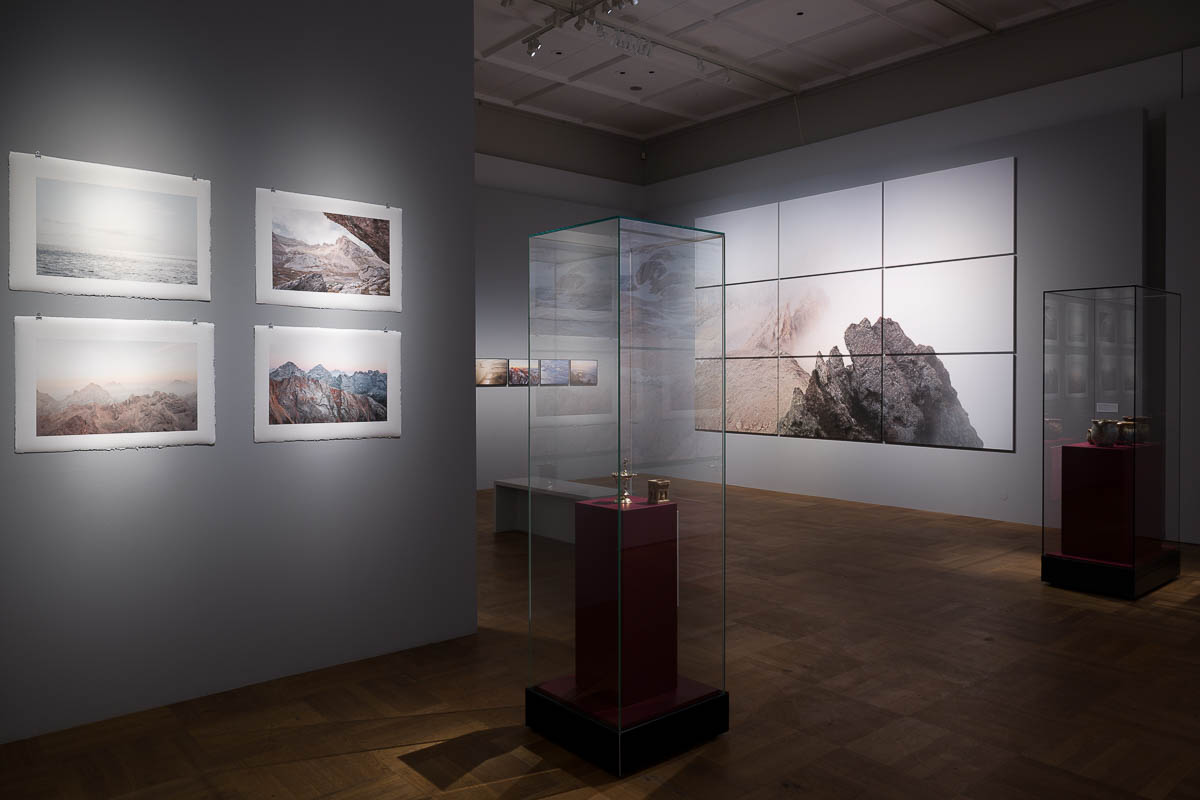Ausstellungsraum mit Fotografien von Dolomiten und Wattenmeer sowie Vitrinen im Bayerischen Nationalmuseum