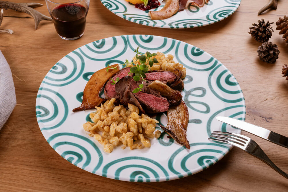 Rosa gebratener Rehrücken mit Spätzle, Kräuterseitlingen und Preiselbeeren auf Teller angerichtet