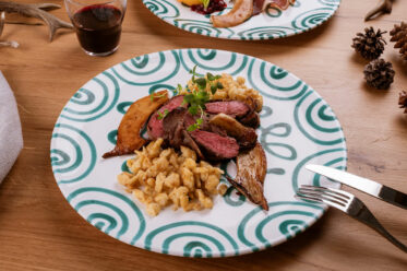 Rosa gebratener Rehrücken mit Spätzle, Kräuterseitlingen und Preiselbeeren auf Teller angerichtet
