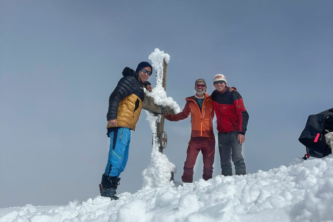 Enno Kapitza und zwei Begleiter am verschneiten Gipfelkreuz des Hocharn bei einer Skitour in den Alpen