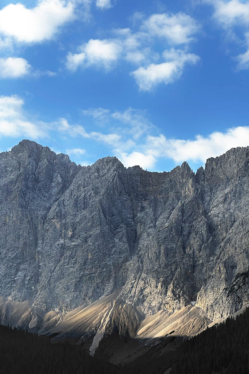 Schroffe graue Felswände und Gipfel im Karwendel unter blauem Himmel und weißen Wolken.